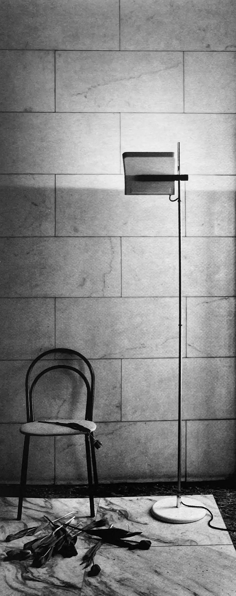 Lampada da terra alogena 1105 accanto a una sedia; foto in bianco e nero, Arteluce Flos