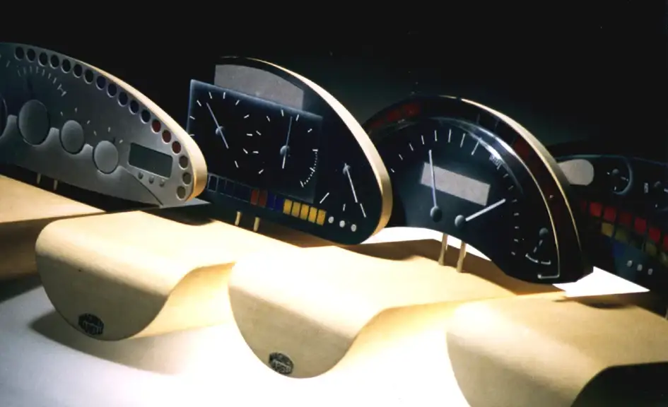 Quattro modelli di cruscotto per automobile con strumenti diversi, allineati su supporti, Magneti Marelli