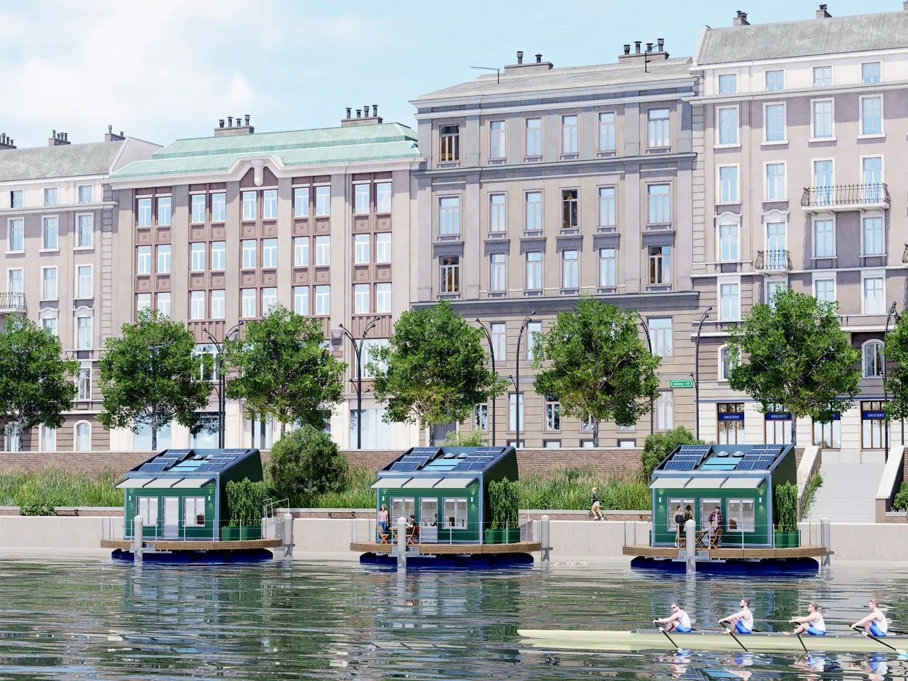 Tre case galleggianti con i pannelli solari sul tetto, ormeggiate lungo la riva di un fiume davanti ai palazzi della città