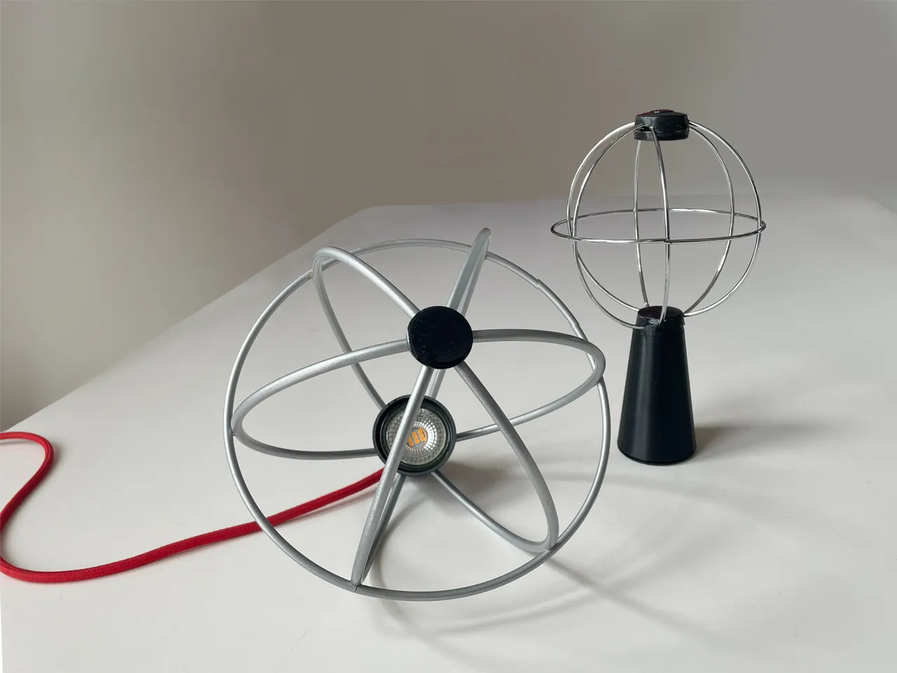 I due prototipi funzionanti: in primo piano la sfera da terra con il faretto LED e il cavo rosso, dietro la versione da tavolo sulla base conica nera