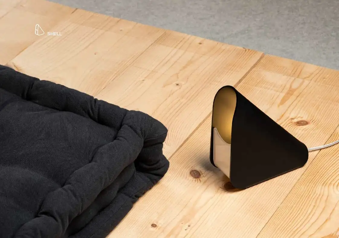 Lampada Shell nera a forma di cono piegato, appoggiata su un pavimento in legno, Vesta