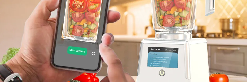 Lo smartphone inquadra le verdure nel bicchiere del frullatore; sul display compare la ricetta del gazpacho