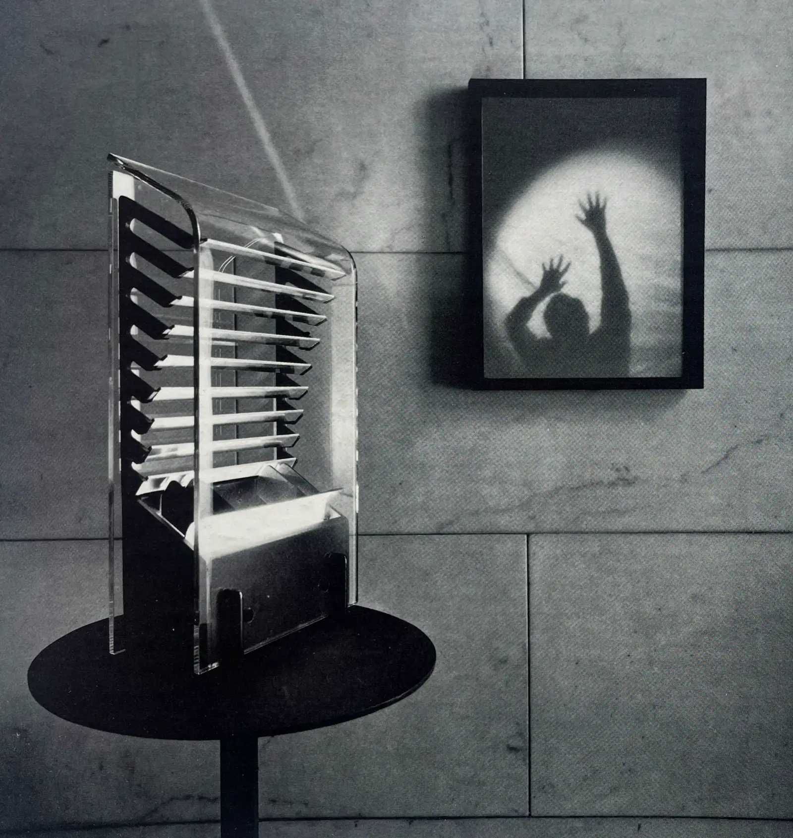 Lampada da tavolo Veneziana con schermo a lamelle, accanto a un quadro con un’ombra; foto in bianco e nero, Arteluce Flos